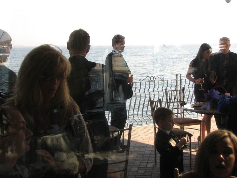People at an event on a patio overlooking the ocean; some are holding drinks.