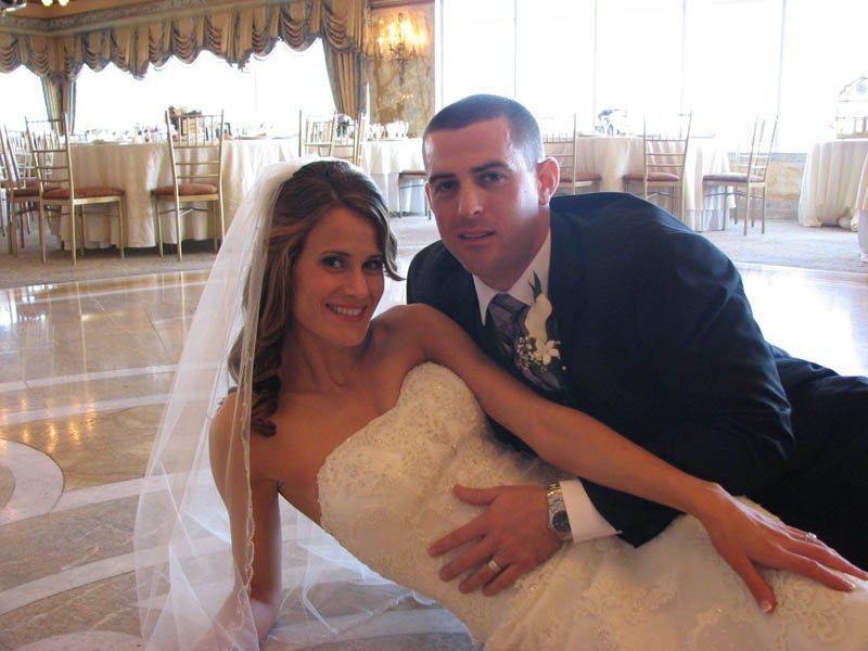 Bride and groom pose on dance floor at wedding reception; bride leans, groom lies next to her.