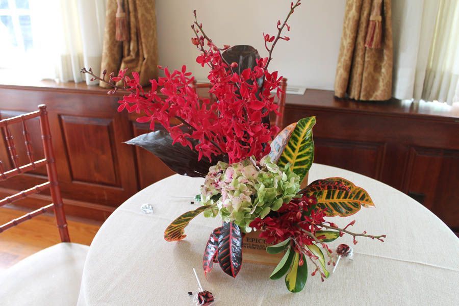 Floral arrangement on a round table. Red orchids, green hydrangeas, and colorful leaves against a wooden background.