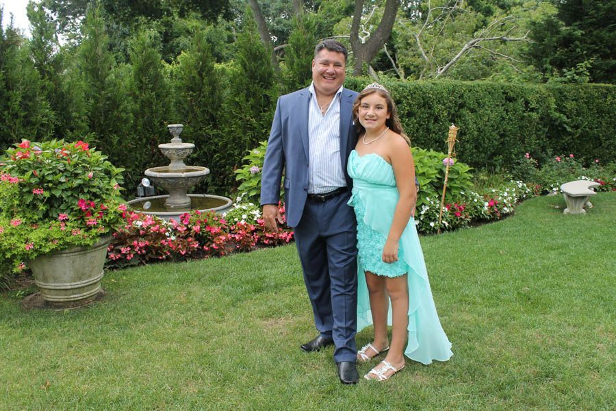 Man and young person in a garden posing next to a tiered fountain, the young person wearing a turquoise dress.