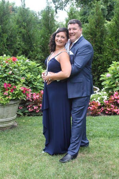 Couple in formal attire embracing in a garden with greenery and colorful flowers.
