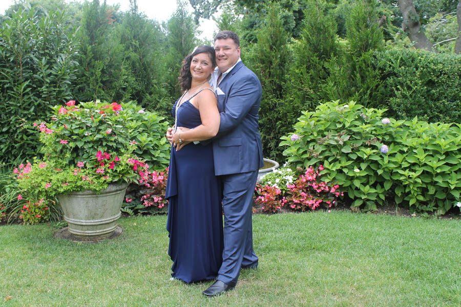 Couple in formal wear embraces outdoors. Man in blue suit, woman in blue gown. Garden setting.