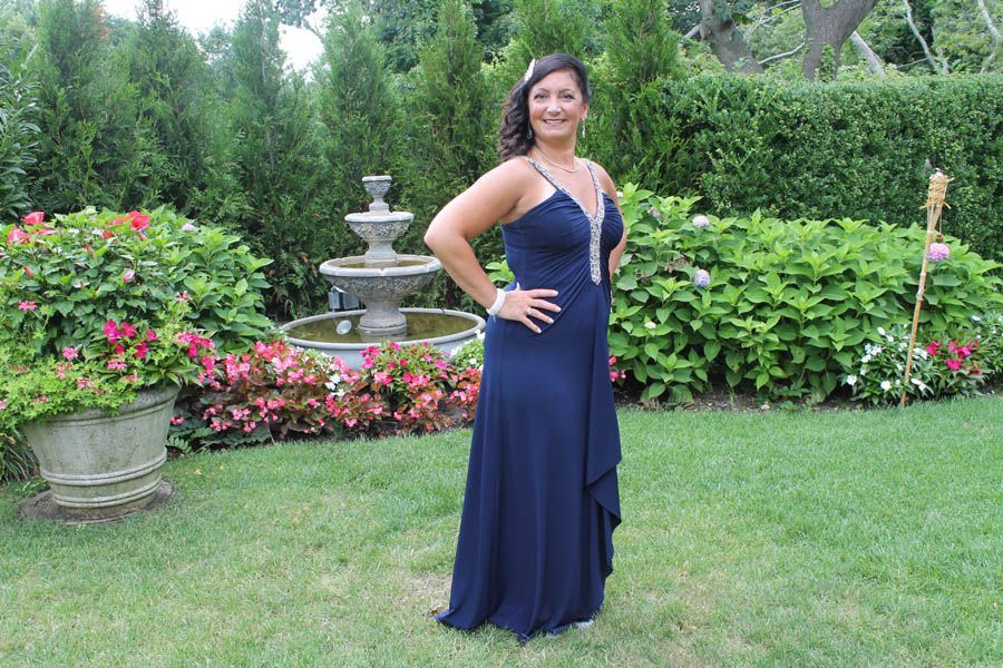 Woman in a navy blue formal dress stands in a garden with a fountain and bushes.