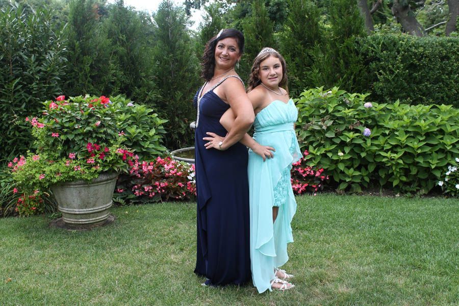 Two women in formal dresses back-to-back in a garden.