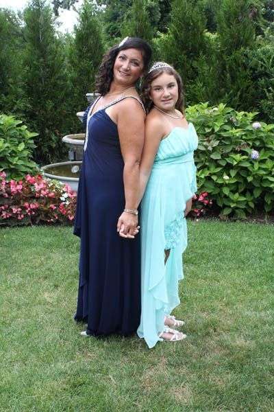 Two women in formal dresses holding hands, standing back to back in a garden.