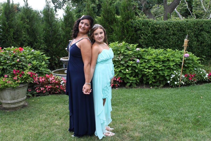 Two people in formal dresses holding hands, standing back to back in a garden.