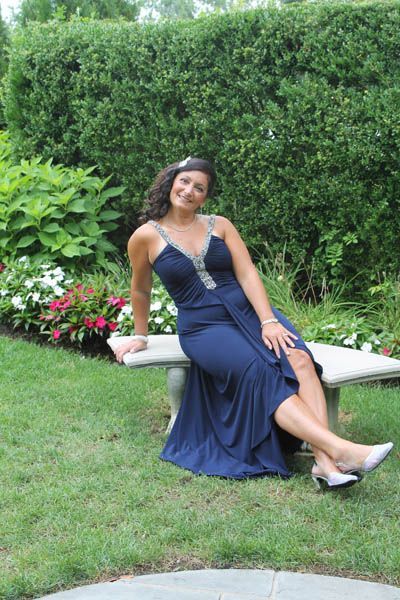 Woman in blue dress sits on a bench in a garden, smiling.