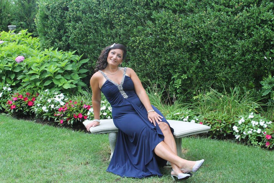Woman in blue gown sits on stone bench in garden.