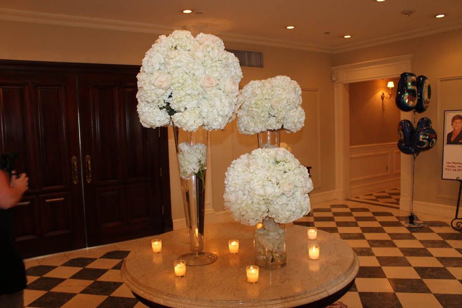 Floral centerpieces on a round table, lit candles, celebration.