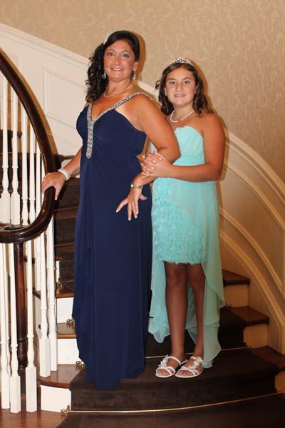Woman in navy dress and girl in aqua dress on a staircase. Both are smiling, girl has a tiara.