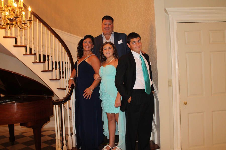 Family of five poses on a staircase with a piano. They are dressed up.