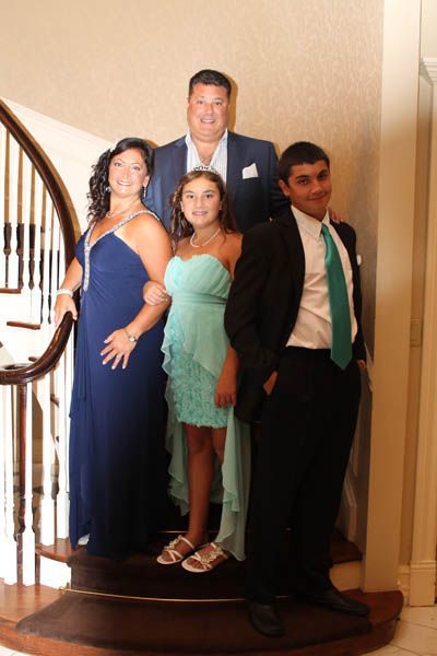 Family in formal attire on a staircase: adults in blue, teens in turquoise and black suits, posing for a photo.