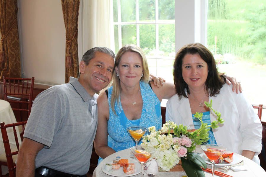 Three people smiling at a table with drinks and flowers by a window.