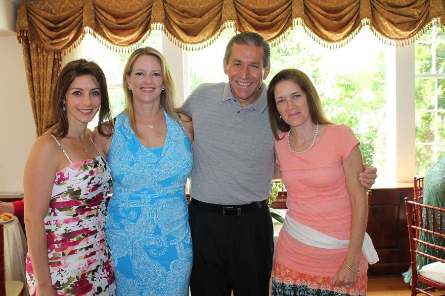Four people smiling, posing together indoors near a window, with a gold curtain backdrop.