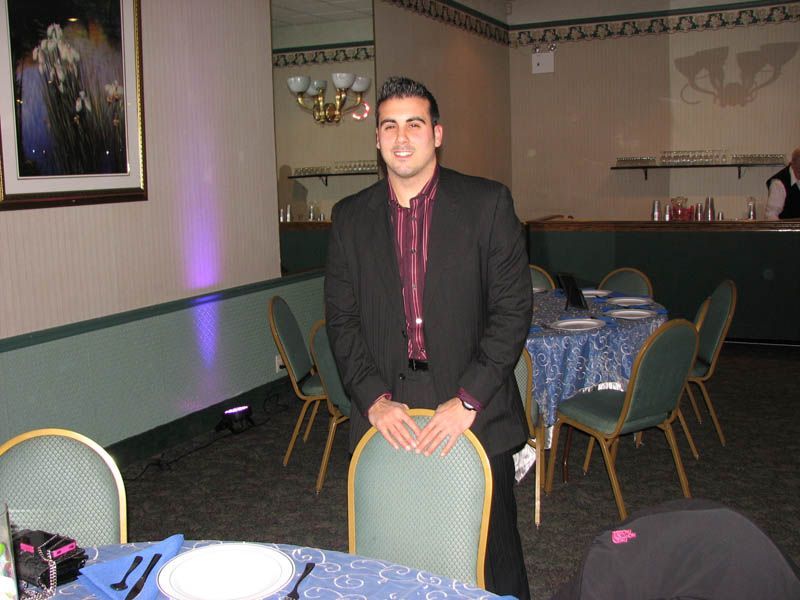 Man in suit stands near a table in a banquet hall, smiling.