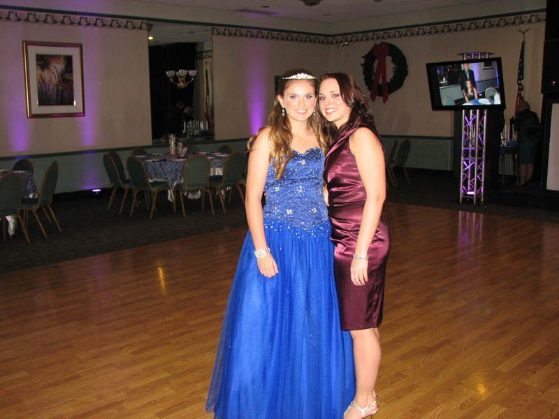 Two women pose in a ballroom: one in a blue gown, the other in a burgundy dress.