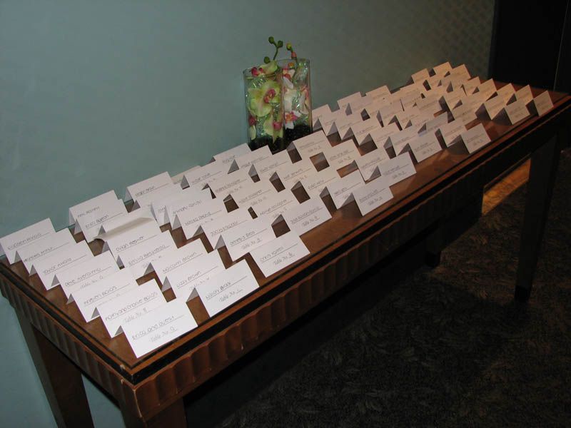A table displaying many place cards, likely for a wedding or event, with a small flower arrangement in the center.