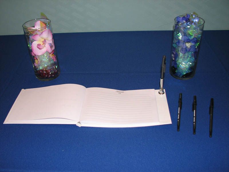 Guest book with pens, flanked by floral vases on a blue table.