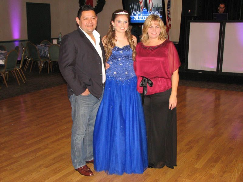 Family poses together, daughter in blue gown, parents smiling, in a ballroom.