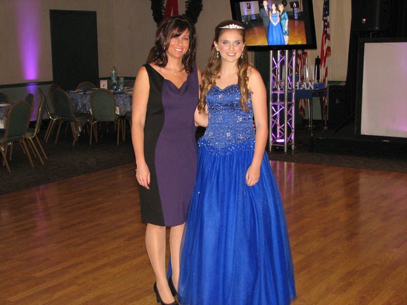 Woman in purple dress and girl in blue gown stand together in a ballroom.