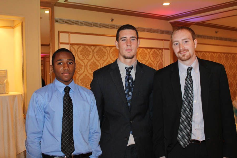 Three men in suits and ties stand indoors, posing for a photo.