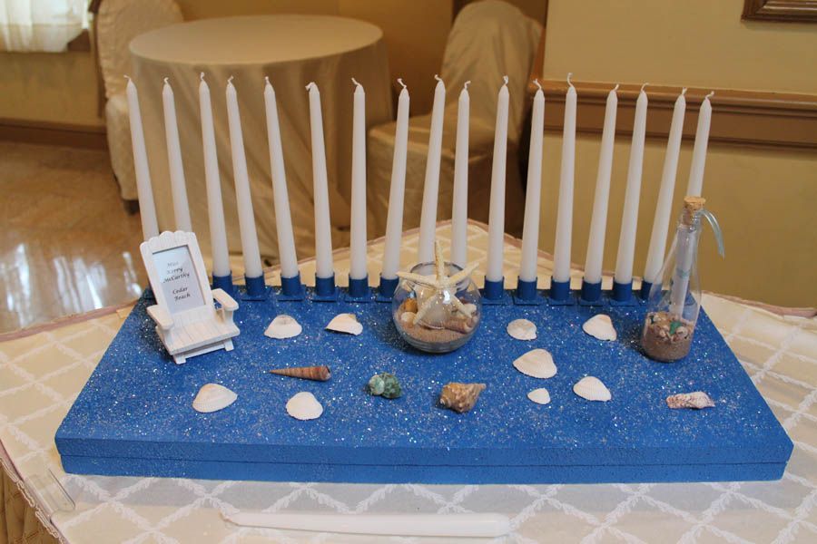 A beach-themed candle display. Blue base with white candles, shells, sand, and nautical decor.