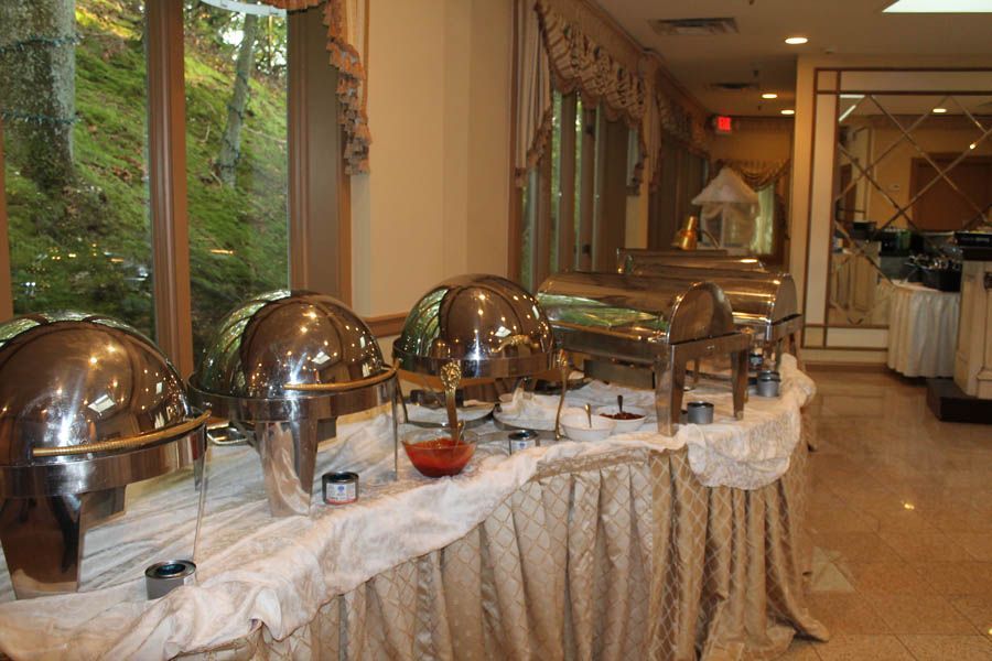 Buffet with silver serving dishes on a draped table, near a window overlooking a wooded area.