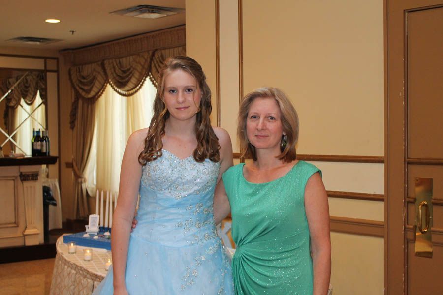Woman and young person pose in formal attire, indoors. Woman wears green dress, young person in blue gown.