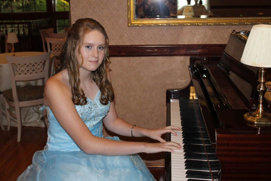 Young person in a blue gown playing piano in a room with a mirror and lamp.