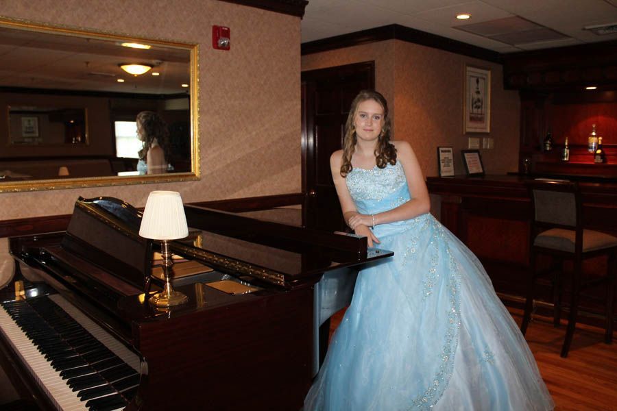 Woman in blue formal dress leans on a piano. Interior with mirror, bar, and lamp.