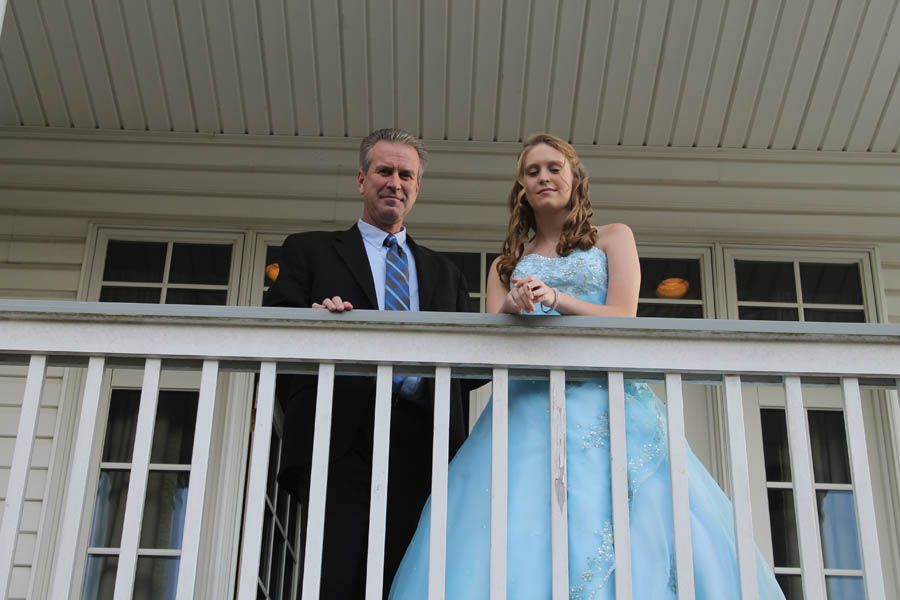 Man in suit and girl in blue gown on a porch, smiling.