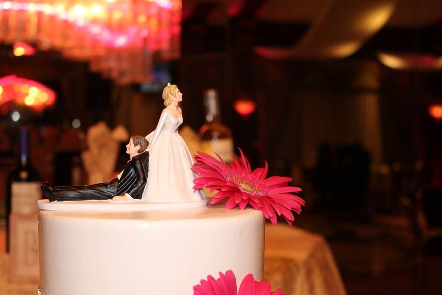 Wedding cake with bride and groom topper, red flower, indoor reception.