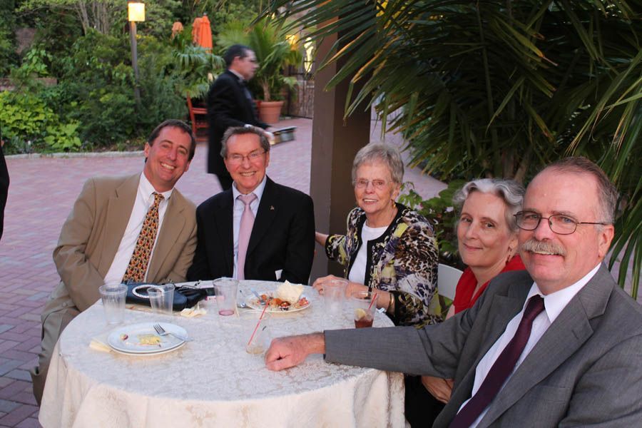 Group of people at an outdoor event seated around a table, smiling.