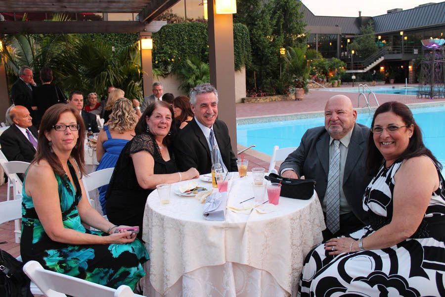 Guests seated around a table by a pool, at an outdoor event. People are smiling and socializing.