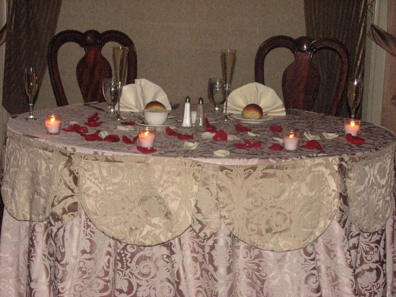 Romantic table set for two, with candles, rose petals, and bread rolls.