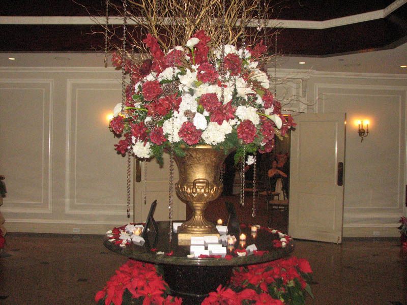 Large floral arrangement in golden urn atop a table, red and white flowers, with Christmas decorations.