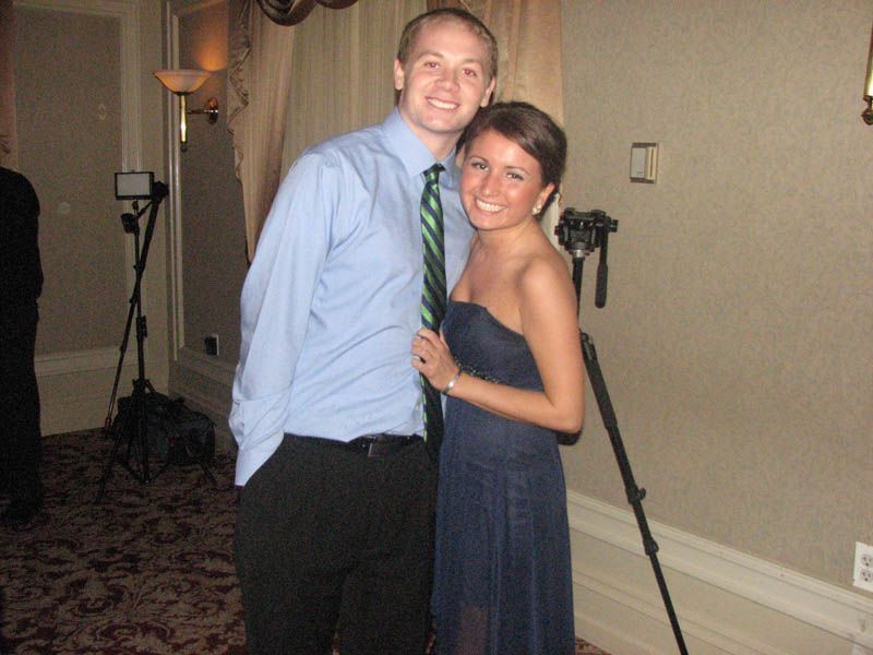 Man in blue shirt and woman in blue dress pose, smiling, indoors near a camera on a tripod.
