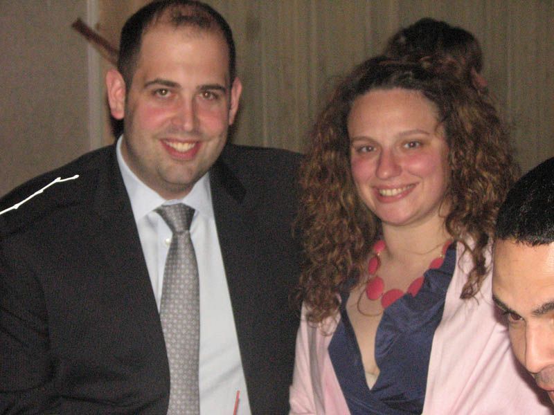 Man and woman smiling, indoors. Man in suit, woman in dress with pink shawl, close-up.