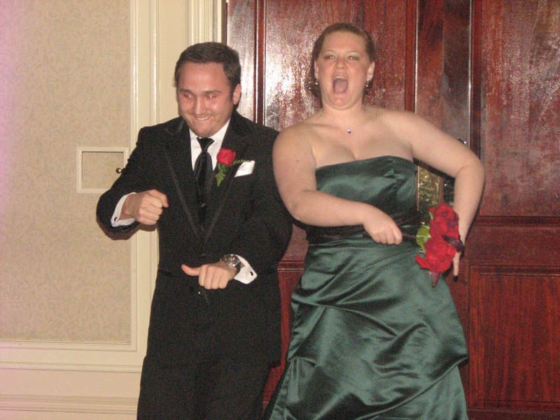 Man and woman in formal wear, dancing with excited expressions, indoors.
