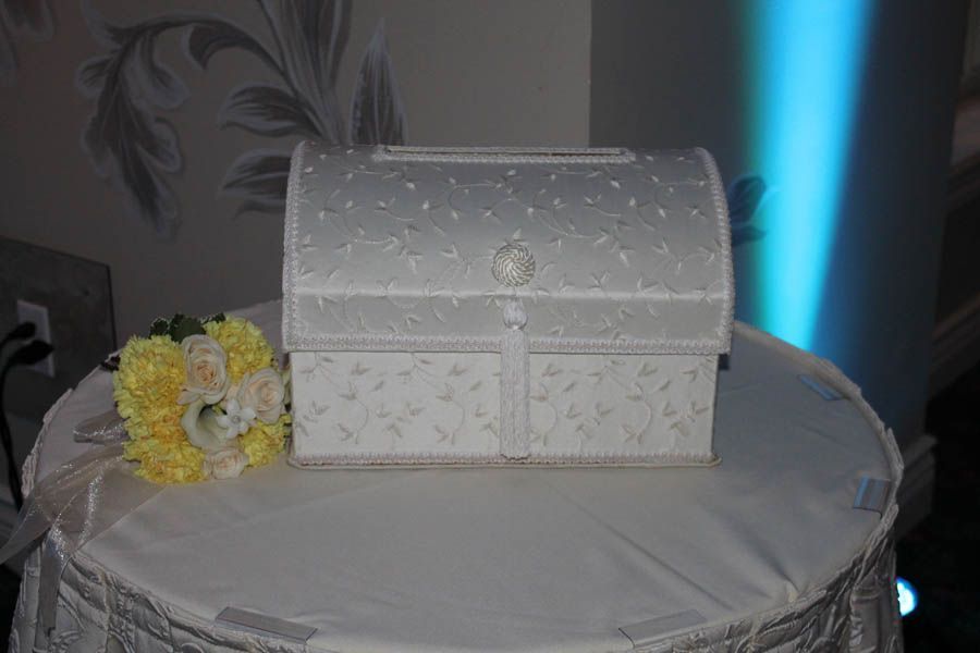 White decorated card box on a round table, with a bouquet of flowers next to it.