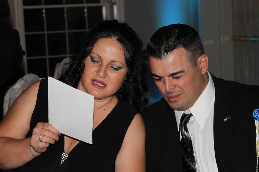 Woman in black dress reads a card while man in suit looks on; both at a formal event.