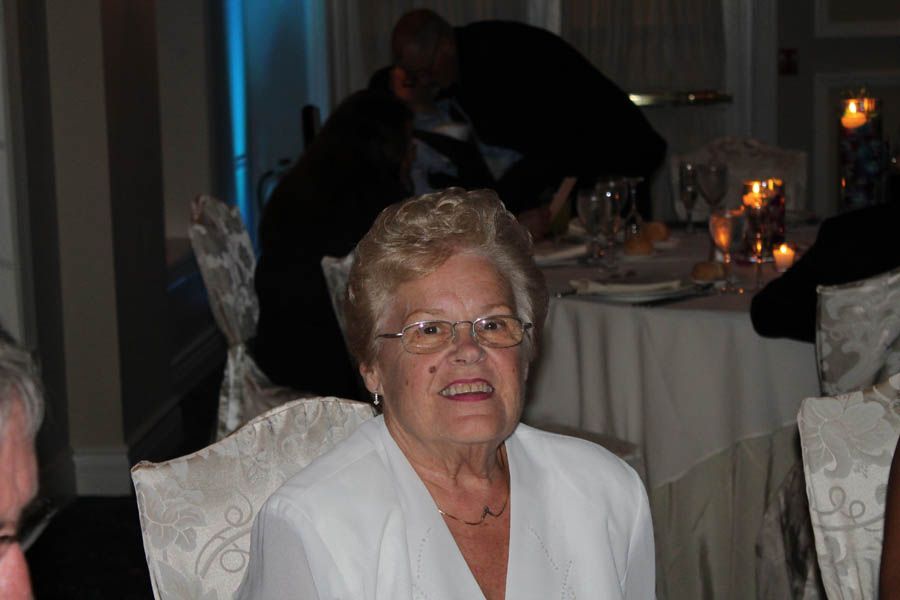Woman with glasses at a formal event, smiling. Other guests and table setting in background.