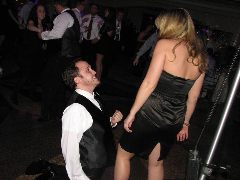 Man kneeling, looking up at woman in black dress on dance floor.