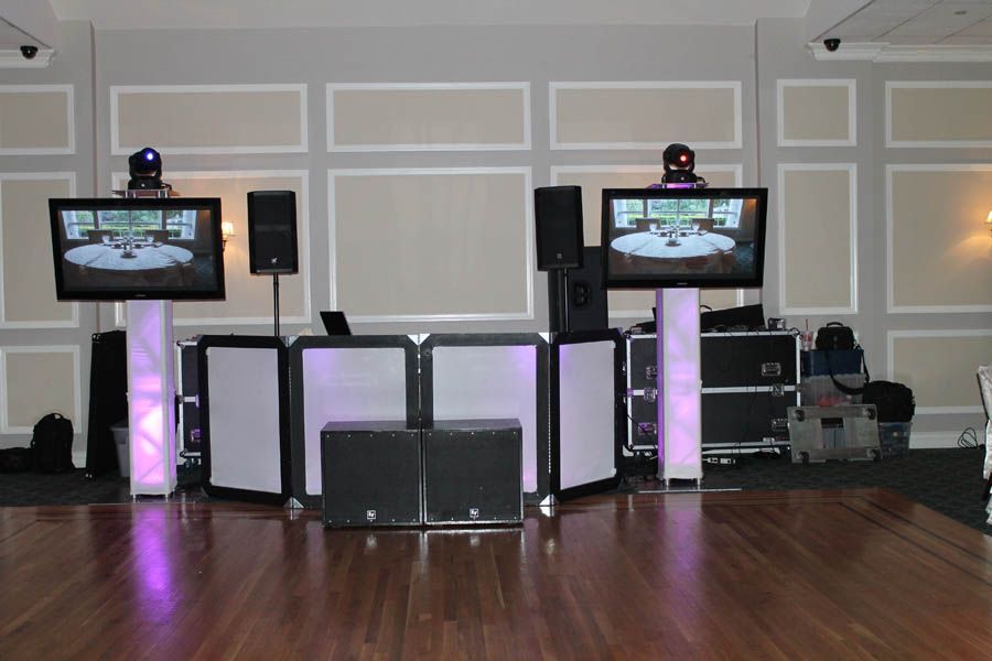 DJ setup with monitors and speakers in a ballroom. Purple uplighting illuminates the front of the stage.
