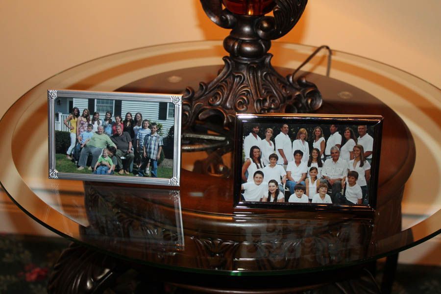 Two family photos in silver frames on a glass-topped table, near a lamp.