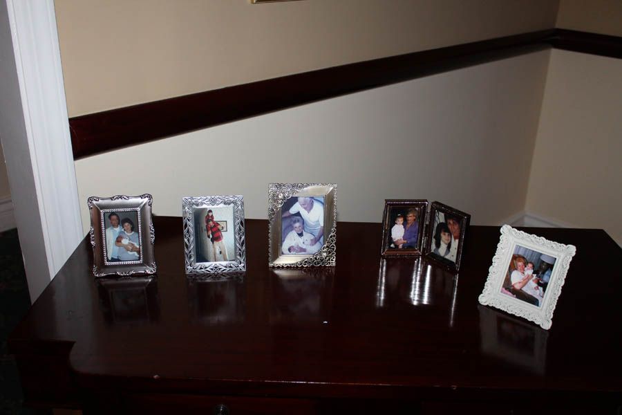 Six framed photos on a dark brown table in front of a white wall and dark brown railing.