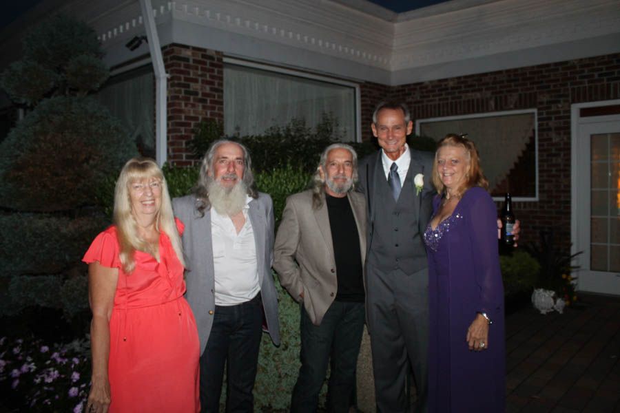 Five people posing for a photo outside a building; a man in a suit, two with beards, two women in dresses.