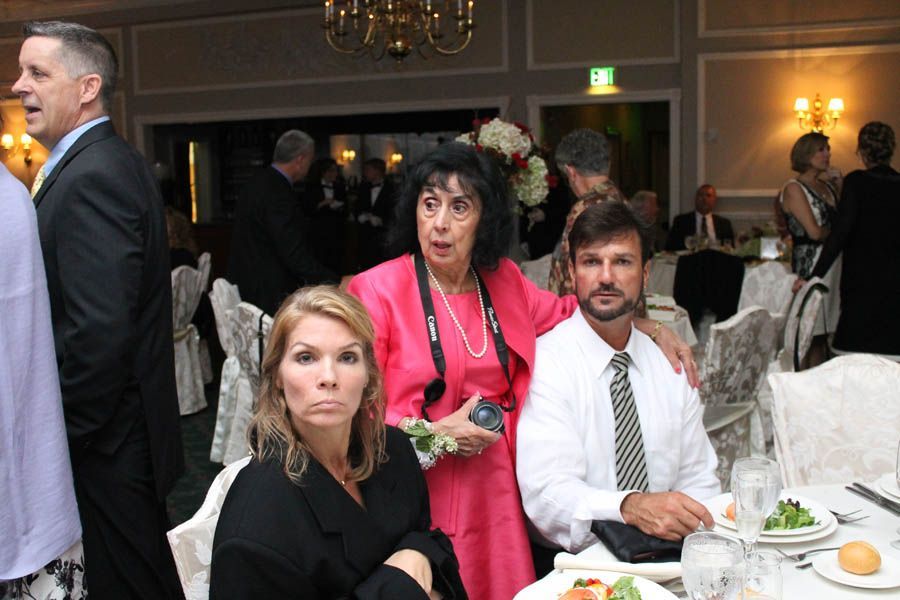 People at a formal event; woman in pink talking, others at tables, dining.
