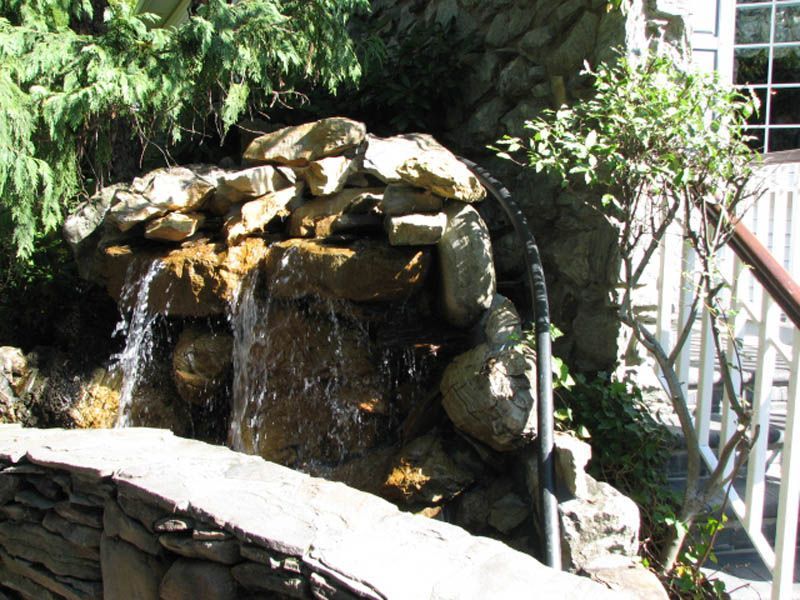 Waterfall feature made of rocks and cascading water, with foliage and a railing nearby.