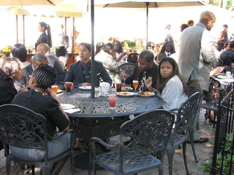 People seated around outdoor tables, eating and conversing under umbrellas.
